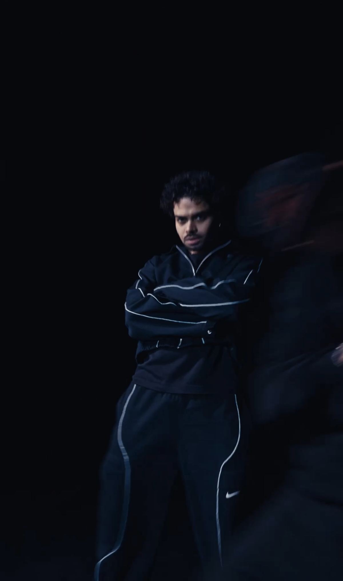 Donovan en survêtement noir, saisi dans un flou de mouvement sur fond sombre.