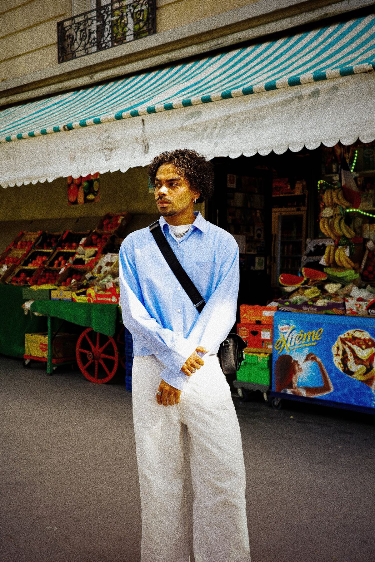 Donovan en chemise bleue devant l’étal coloré d’un primeur parisien.